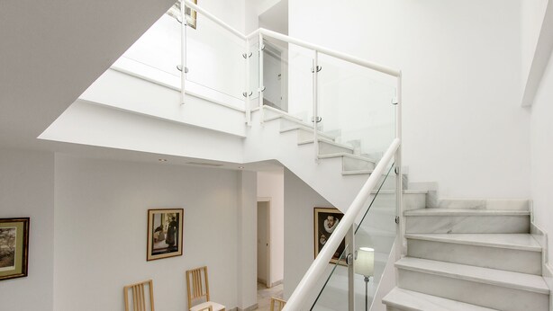 Un interno moderno con una scala in vetro, pareti bianche e opere d'arte incorniciate.