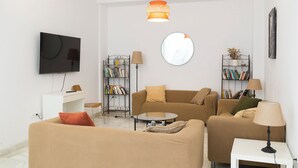Un soggiorno moderno con divano, due poltrone, tavolino, televisore, librerie e uno specchio.