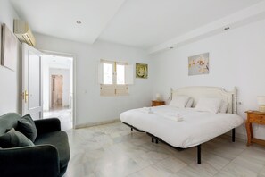 A bedroom with a bed, a nightstand, a chair, and a door leading to another room.