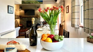 Een eethoek met een tafel gedekt voor twee personen, een fles wijn, een schaal fruit en een vaas tulpen.