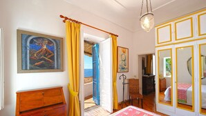 A bedroom with a bed, a wooden dresser, a painting, and a view of the sea. - Casa Angels with shared pool (Positano)