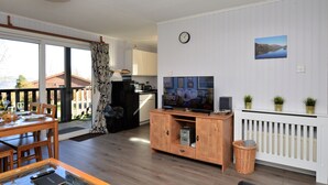A modern living room with a wooden entertainment unit, a television, and a dining area with a table and chairs.