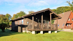 A wooden cabin with a porch, a small deck, and a sloped roof.