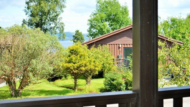 A wooden cabin with a green lawn and trees in the foreground.