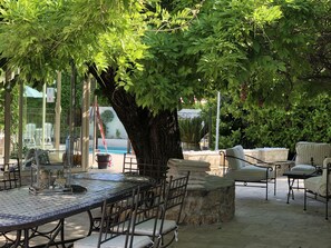 Un'area patio con tavolo e sedie, immersa nel verde e con un grande albero.