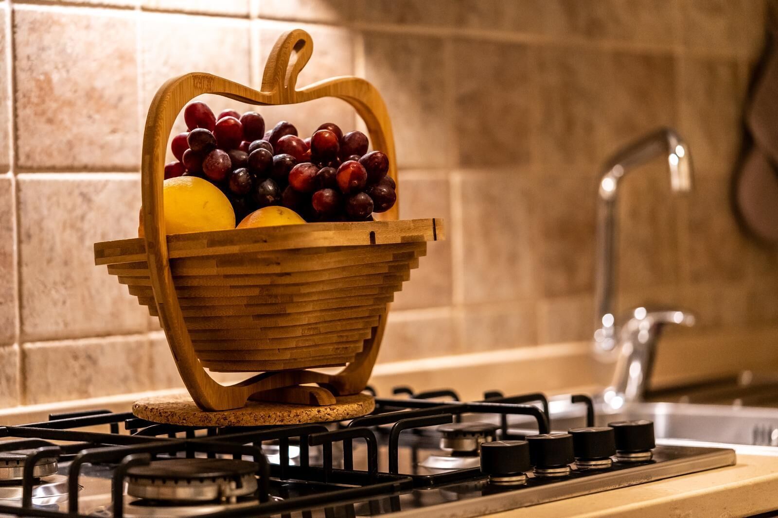 A wooden fruit basket with grapes and oranges on a kitchen stove.