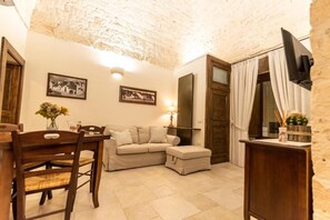 Uma sala de estar aconchegante com uma mesa de jantar de madeira, um sofá bege e uma televisão fixada na parede.