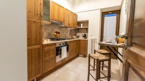 Eine kleine Küche mit Holzschränken, einem Gasherd, einem Backofen und einer Essecke mit Hocker.