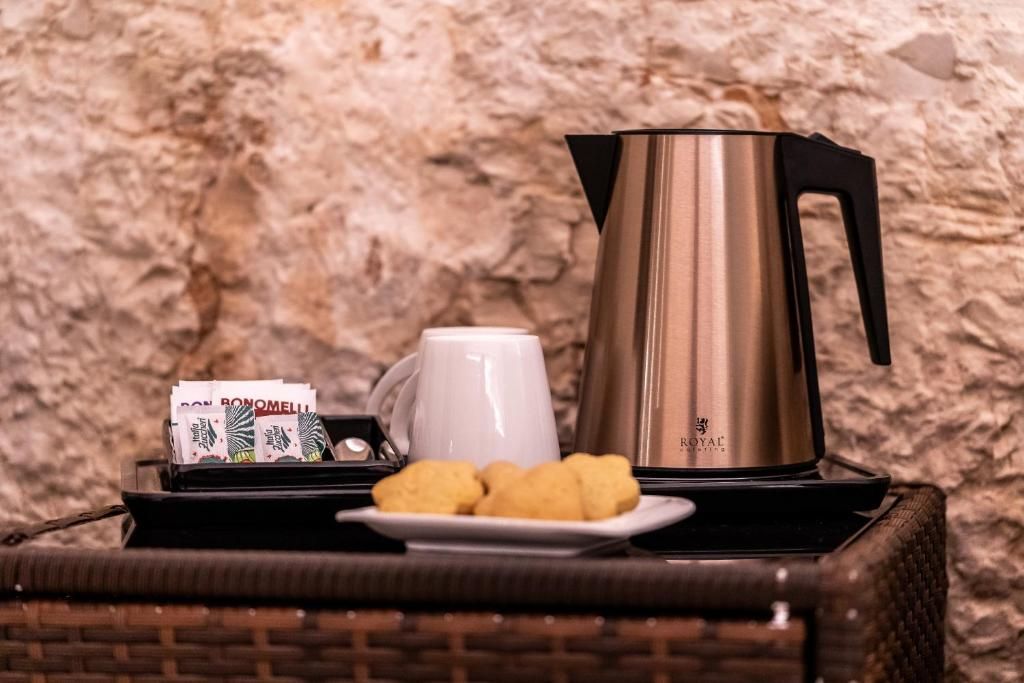 Una bandeja con una cafetera, una taza y galletas sobre una mesa de mimbre frente a una pared con textura.