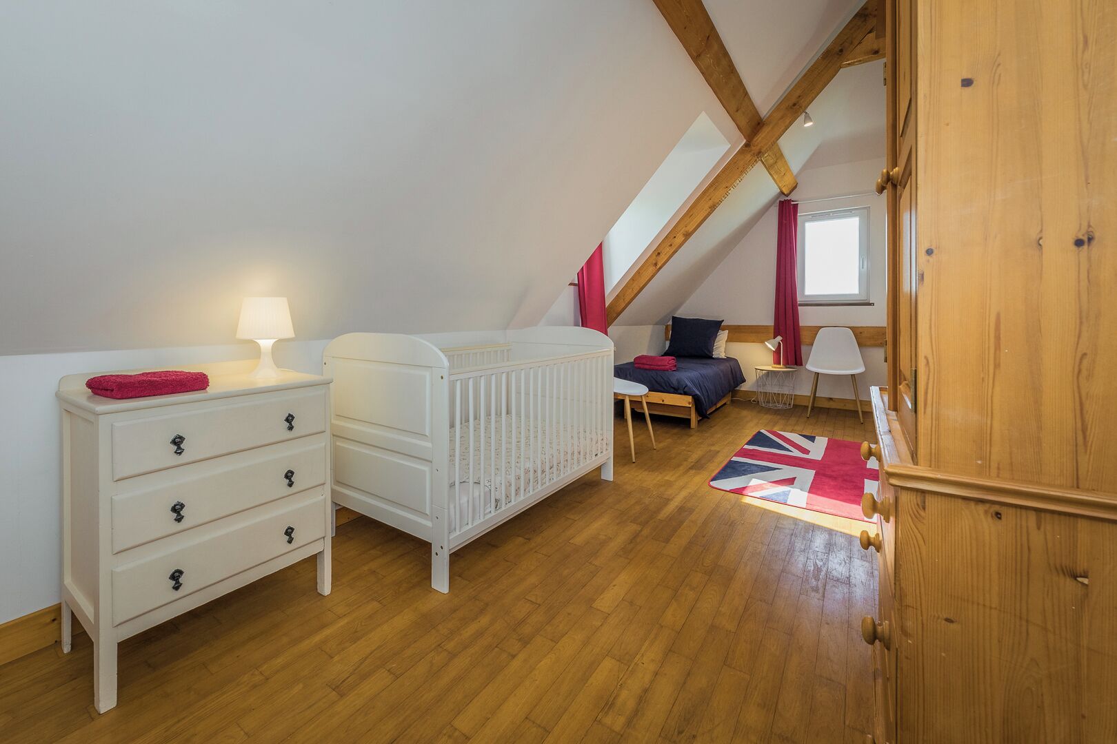 Una habitación infantil con una cuna, una cama, un tocador y una ventana con cortinas.