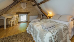 A cozy attic bedroom with a sloped ceiling, a bed with patterned bedding, a desk with a chair, and a fireplace. - Villa Découverte, luxury house with private pool (Reilhaguet)