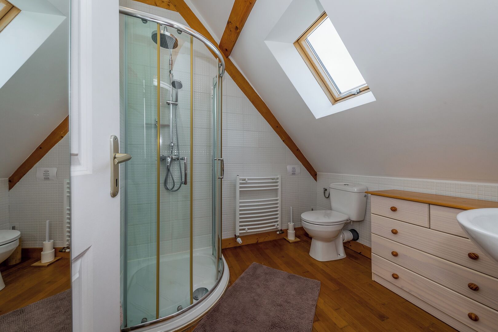 A modern bathroom with a glass shower enclosure, a toilet, a sink, and wooden cabinets.