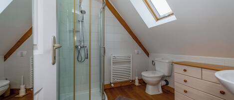 A modern bathroom with a glass shower enclosure, a toilet, a sink, and wooden cabinets.