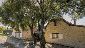 A stone building with a tiled roof, a gravel path, and a tree in front. - Villa Découverte, luxury house with private pool (Reilhaguet)