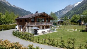 A chalet-style building with a balcony, surrounded by a well-maintained lawn and a mountain backdrop. - Chalet Everest - Lovely brand new 4 bedroom chalet from a walk into town (Chamonix-Mont-Blanc)