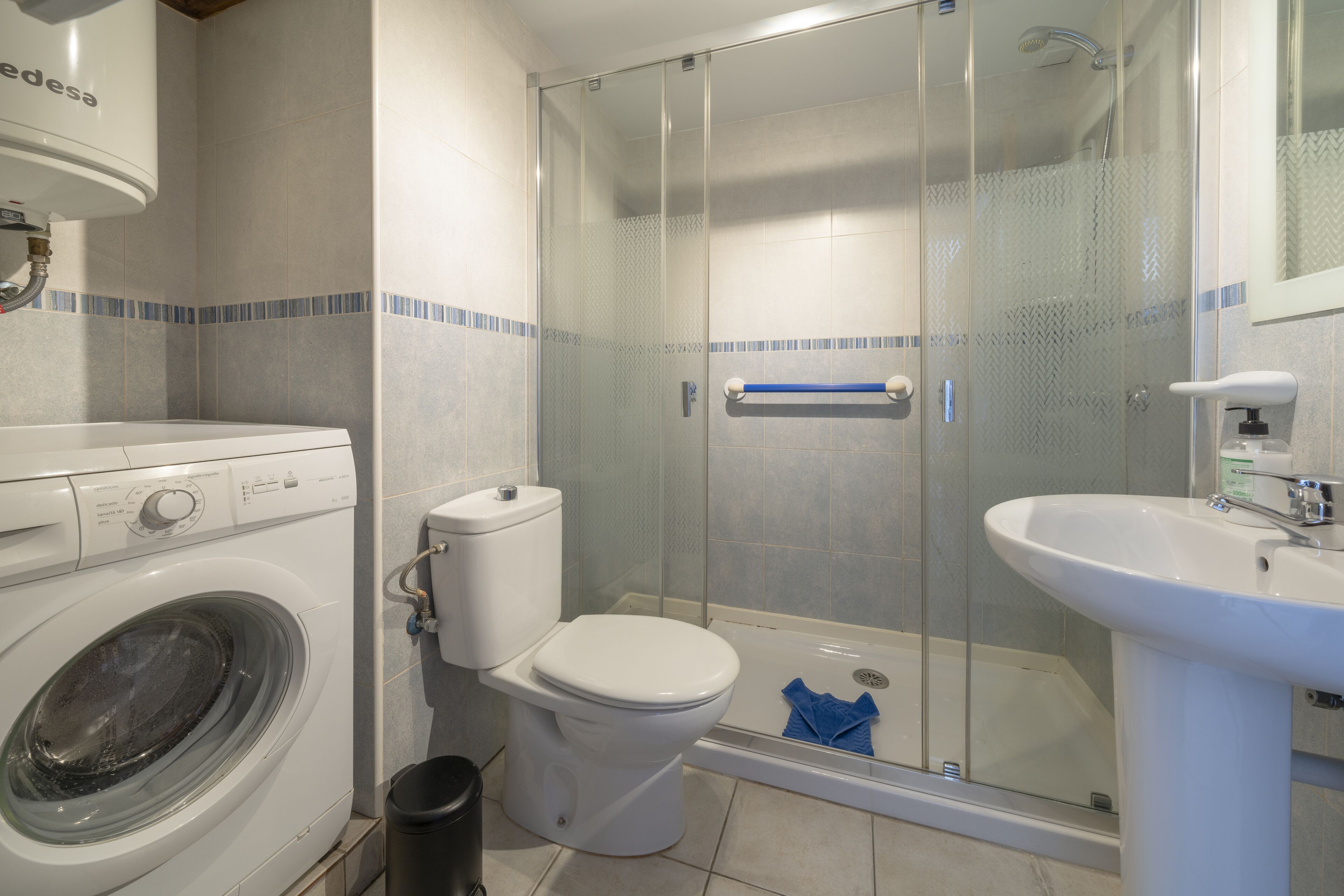 Une salle de bain équipée d’un lave-linge, de toilettes, d’une douche et d’un lavabo.
