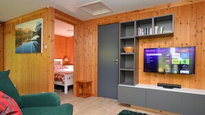 Uma sala de estar com uma parede revestida em madeira, uma TV de tela plana instalada acima de um móvel cinza e um sofá verde.