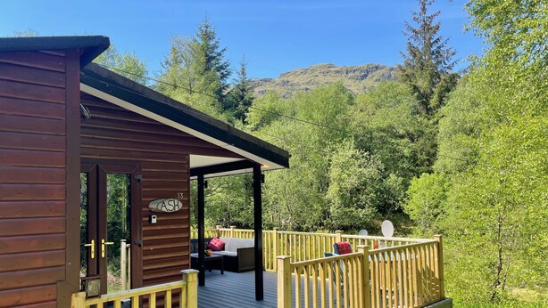Uma cabana de madeira com um deck, uma área de estar coberta e uma placa com o texto 'ASH 13'.