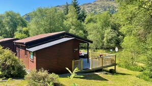 Uma cabana com varanda, rodeada por vegetação e colinas.