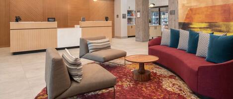 A modern hotel lobby with a reception desk, seating area, and a large abstract mural.