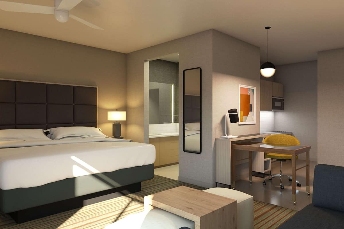 A hotel room with a bed, desk, chair, sofa, and a small table.