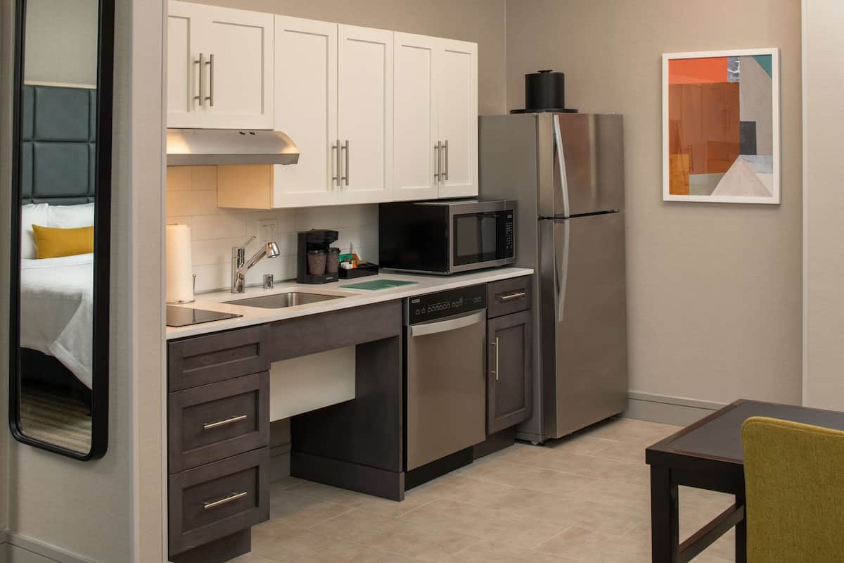 A compact kitchen with white cabinets, a stainless steel refrigerator, a microwave, and a dishwasher.