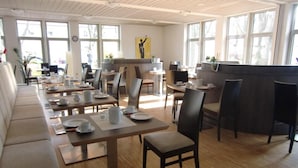 A modern dining area with wooden tables and chairs, large windows, and a central counter. - Kolping Hotel Schweinfurt (Schweinfurt)