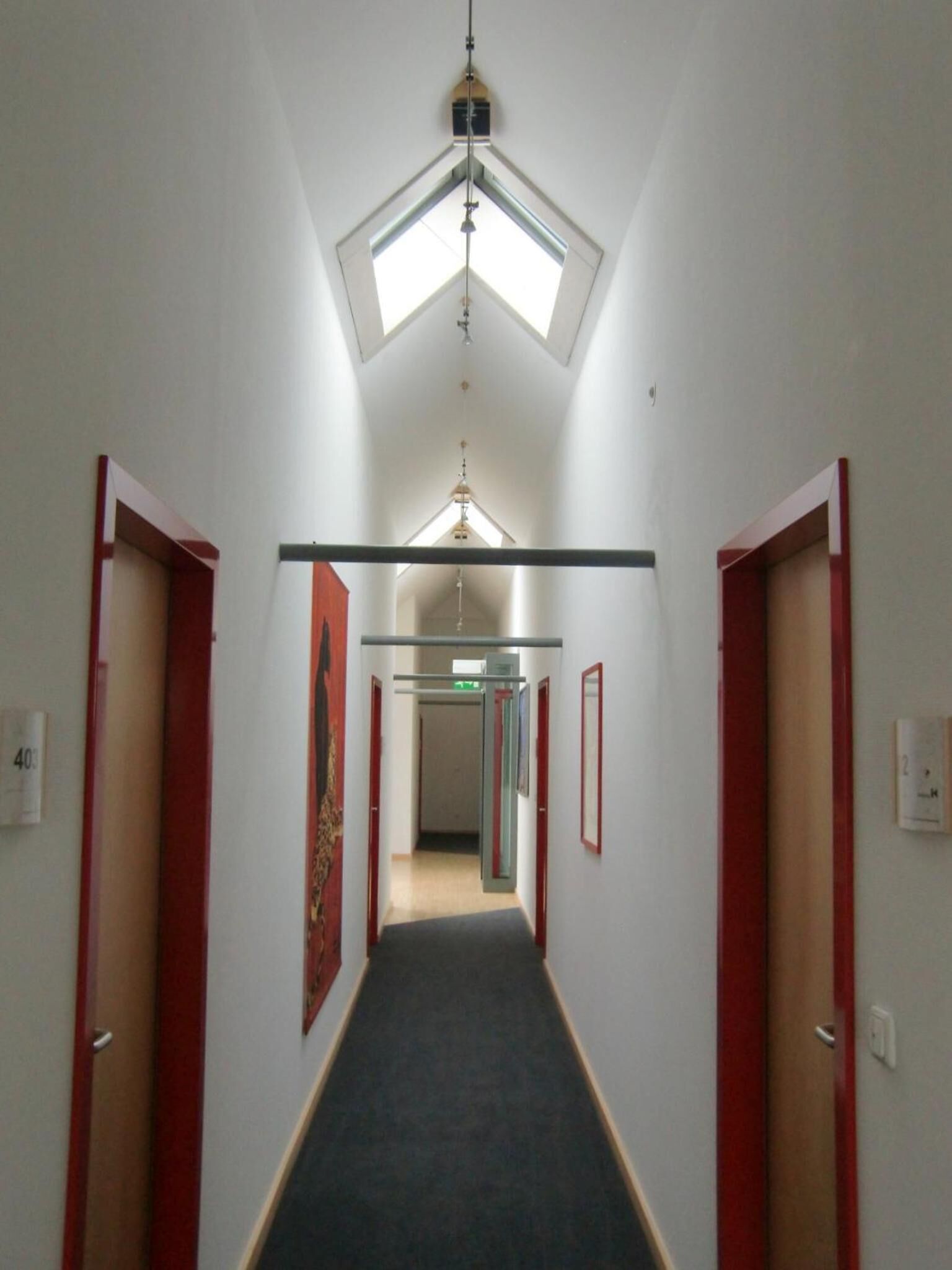A narrow hallway with a skylight, red-framed doors, and a central corridor.