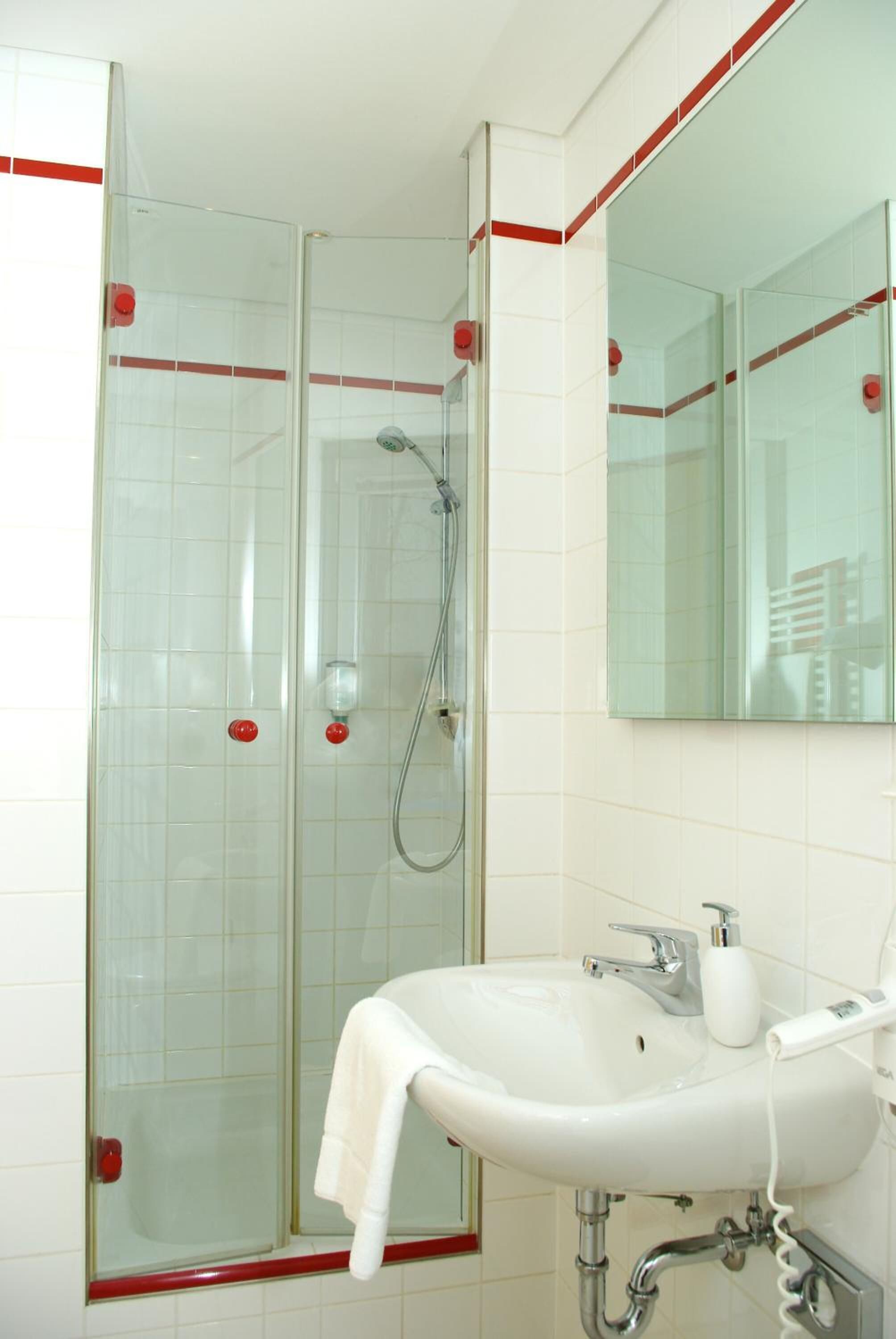 A bathroom with a glass-enclosed shower, a white sink with a mirror above it, and red accents on the walls and shower door.
