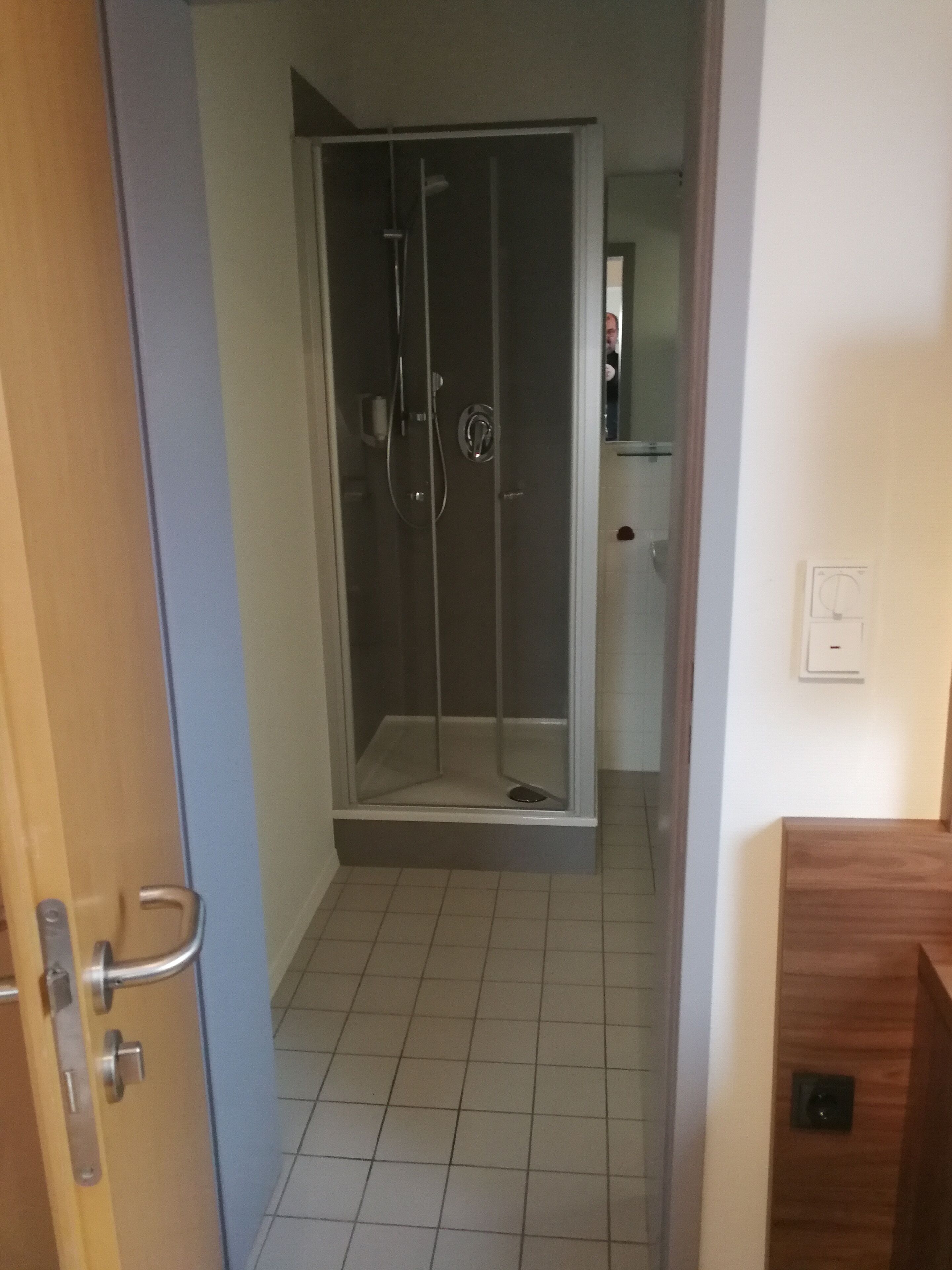 Ein Badezimmer mit Duschkabine aus Glas, einer Holztür und einem Fliesenboden.