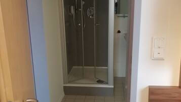 Ein Badezimmer mit Duschkabine aus Glas, einer Holztür und einem Fliesenboden.