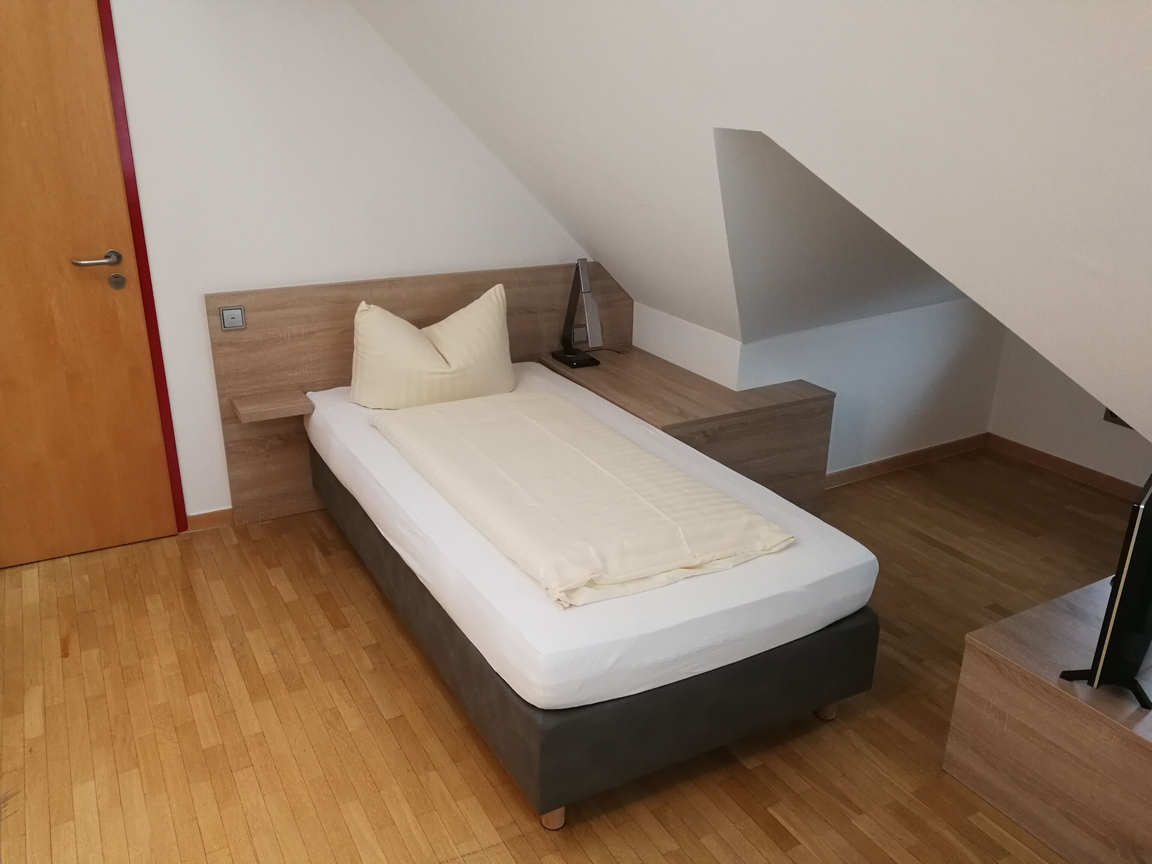 A small, modern bedroom with a bed, bedside table, and a nightstand.