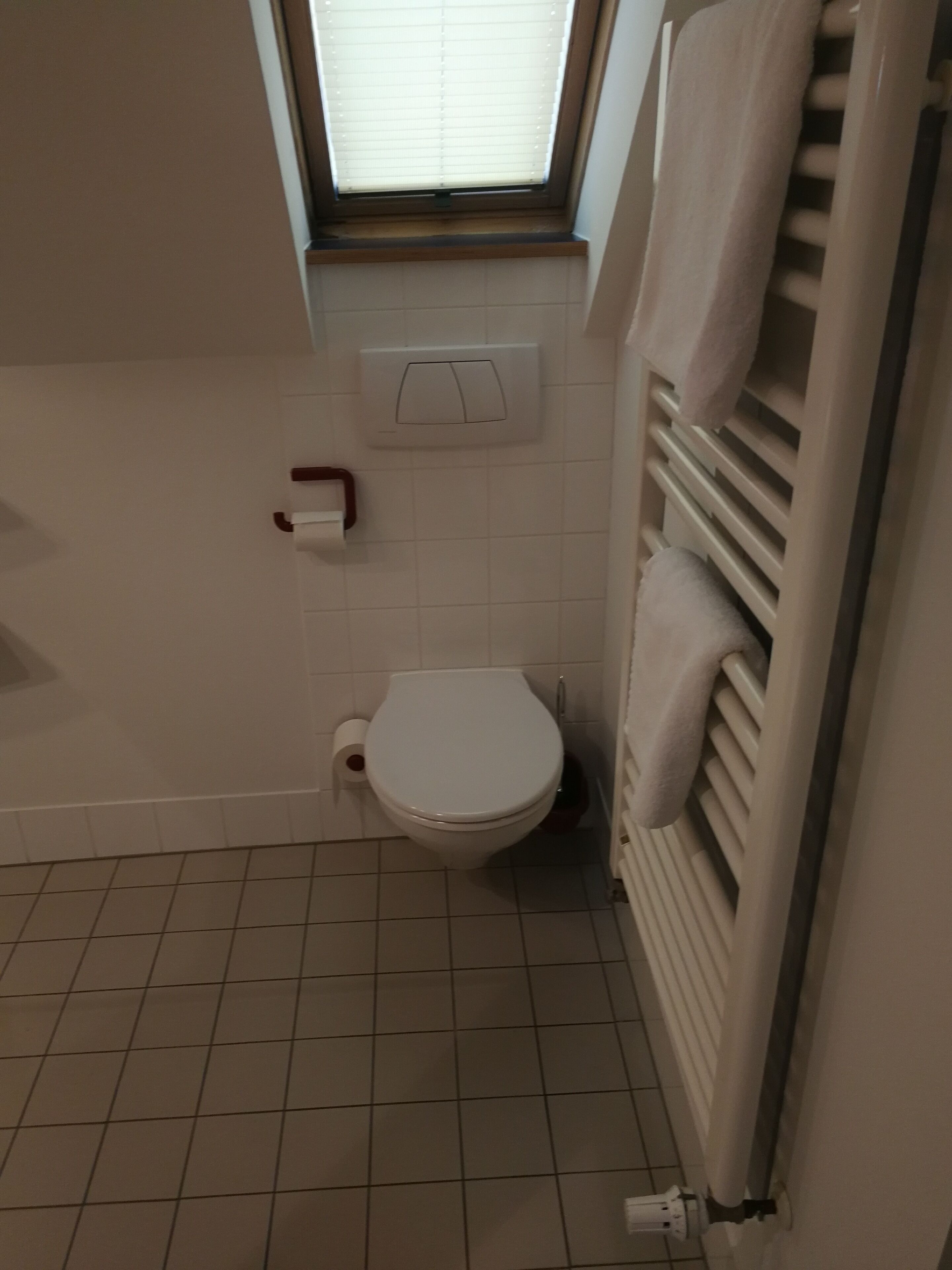 A small bathroom with a toilet, a window, a towel rack, and a toilet paper holder.
