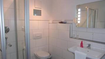 Un baño con cabina de ducha de vidrio, inodoro, lavamanos con espejo y perchero para toallas.
