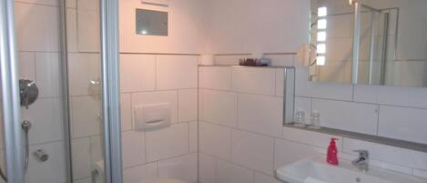 Un baño con cabina de ducha de vidrio, inodoro, lavamanos con espejo y perchero para toallas.