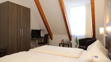 A hotel room with a bed, a desk, a chair, a wardrobe, and a window with curtains.