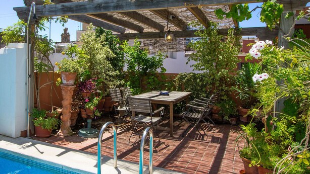 A covered patio with a pool, outdoor seating, and potted plants.