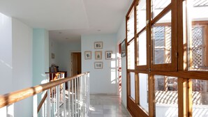 A spacious hallway with a wooden railing, large windows, and a tiled floor.
