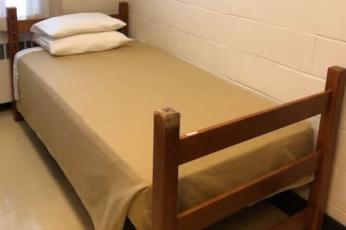 A small, single-bed room with a wooden frame and a beige bedspread.