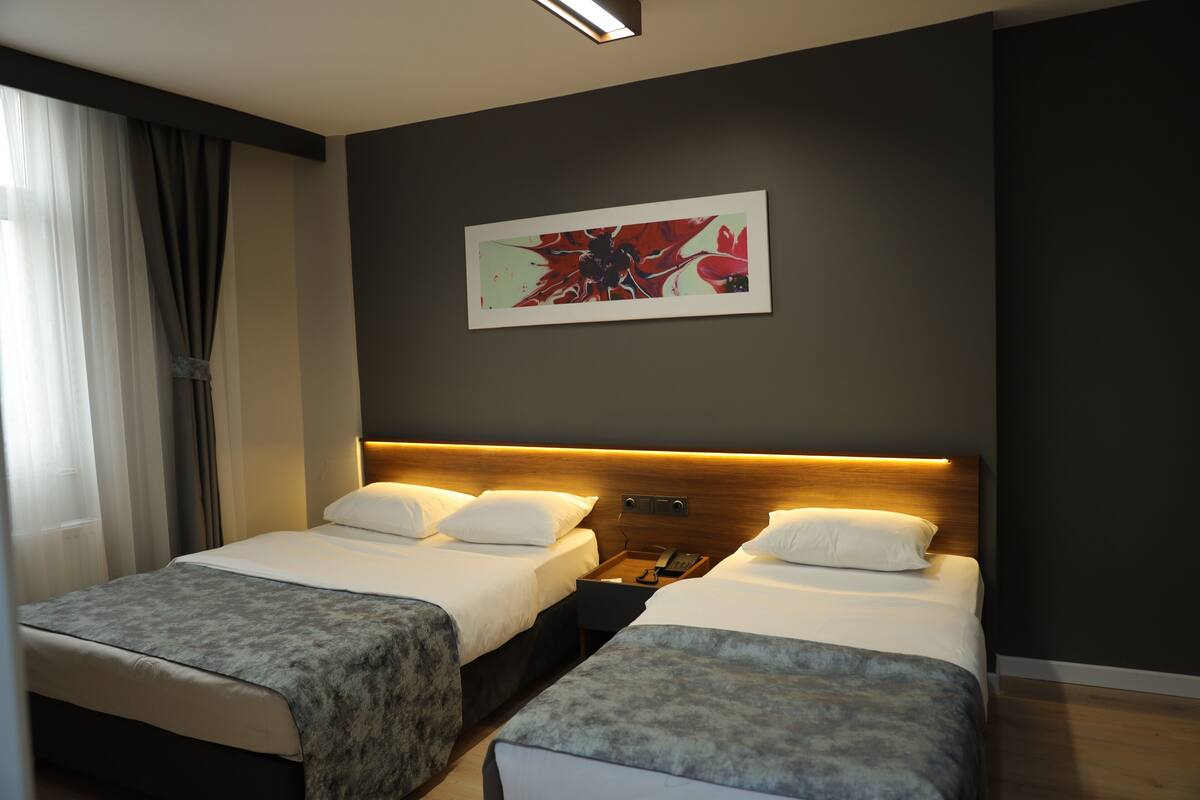A hotel room with two beds, a nightstand, a telephone, and a painting on the wall.