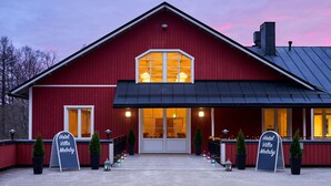 A red barn-style building with a large entrance and two potted trees in front. - Hotel Villa Molnby (Porvoo)