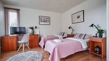 Ett sovrum med två sängar, ett skrivbord med en tv, en stol och ett nattduksbord med en lampa och en växt.
