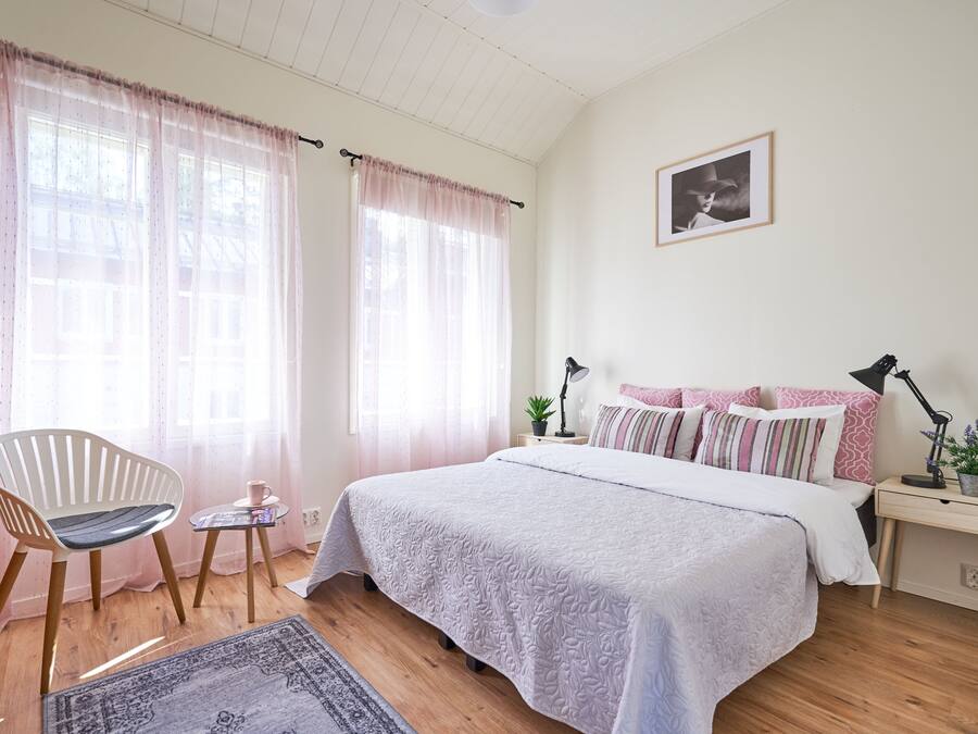 A bedroom with a bed, a chair, a small table, and a nightstand.