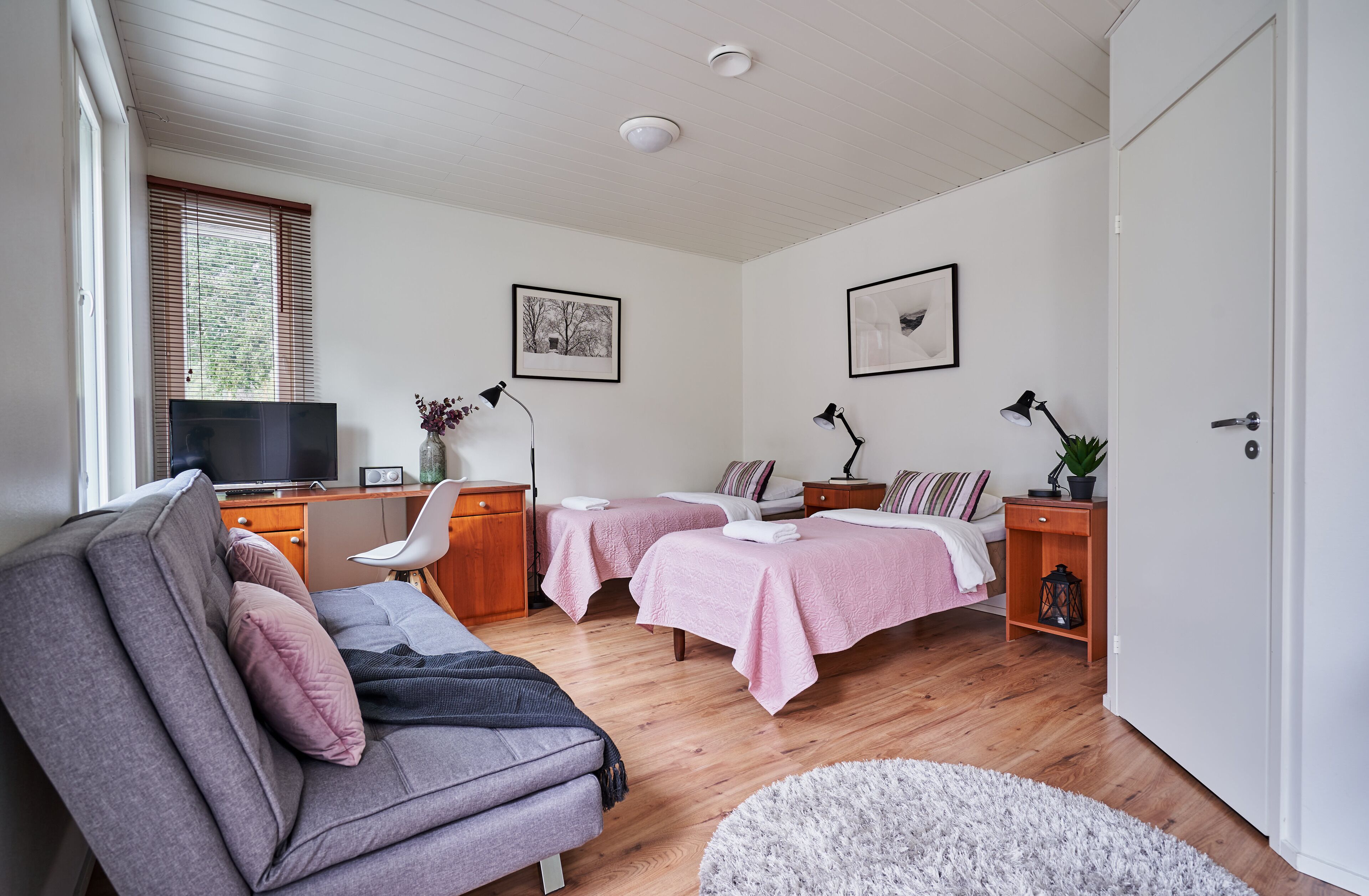 A modern bedroom with two beds, a sofa, a desk, and a TV.