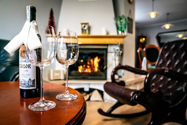 A bottle of KAGOR sweet wine, two empty glasses, a leather chair, and a fireplace with a fire.