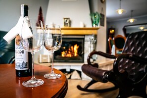 A bottle of KAGOR sweet wine, two empty glasses, a leather chair, and a fireplace with a fire.