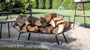 A metal rack holding a stack of firewood in an outdoor setting with picnic tables and neatly trimmed bushes. - are you looking for relaxation, action and culture? (Paszkowka)