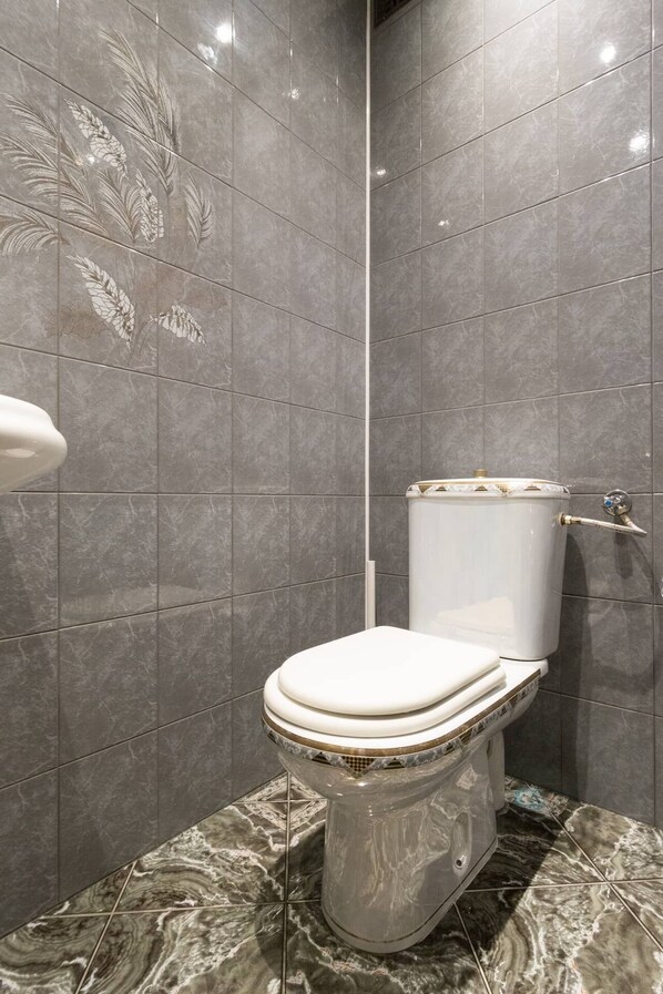 A modern bathroom with a marble floor, a toilet with a gold trim, and a wall with a leaf pattern.