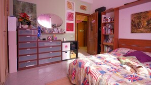 A bedroom with a bed, dresser, and shelves with books and decorations. - Casa Arcobaleno (Rome)