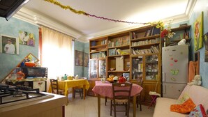 A cozy kitchen with a dining table, chairs, a refrigerator, and a bookshelf filled with books and decorative items. - Casa Arcobaleno (Rome)